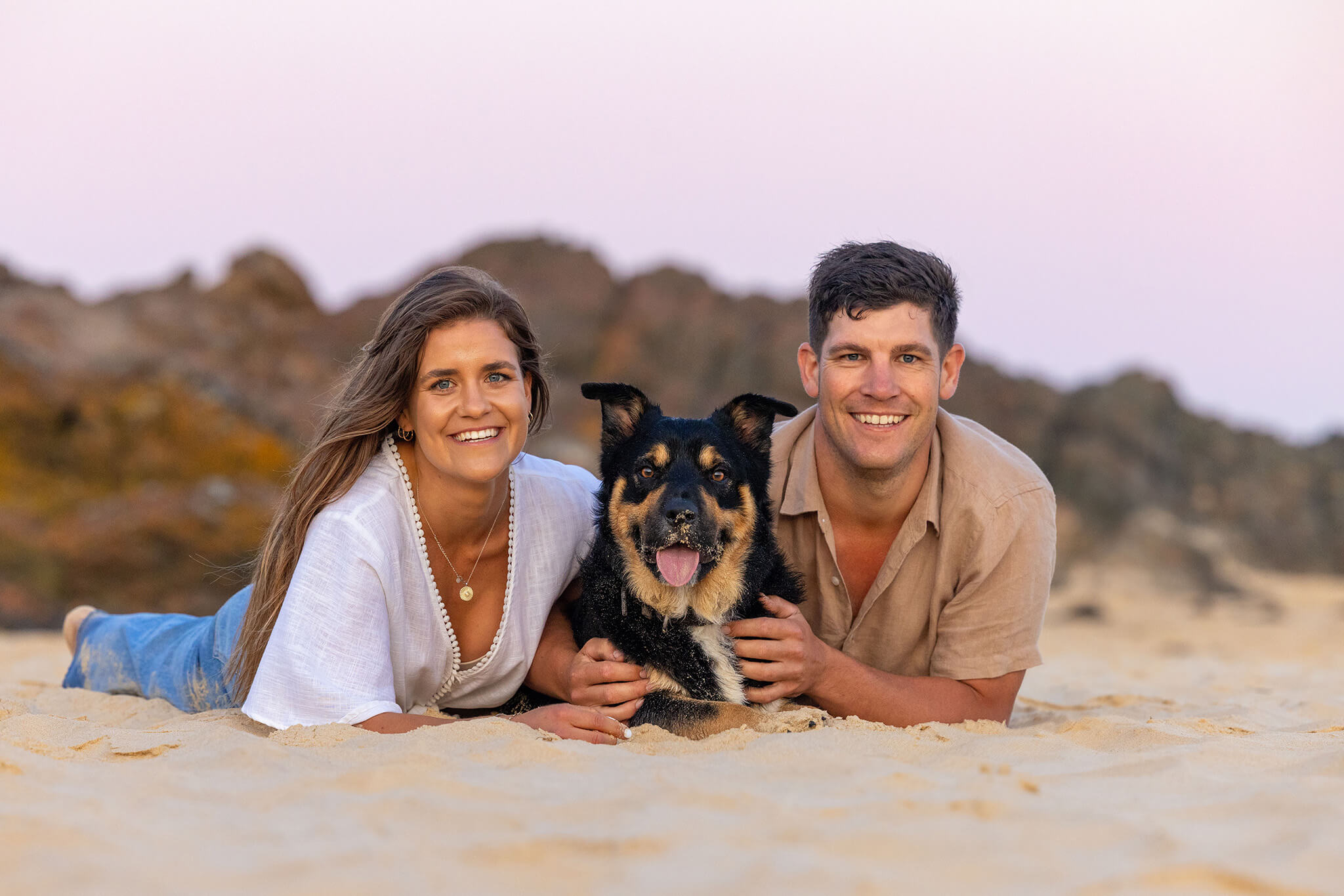 A young couple posing on the sand with their Kelpie x Border Collie Nicho